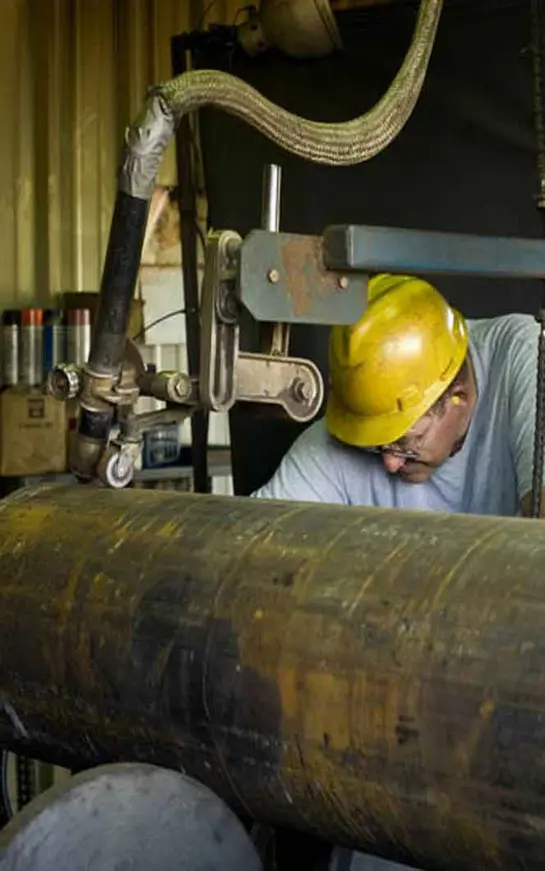 A man in yellow hard hat working on pipe.