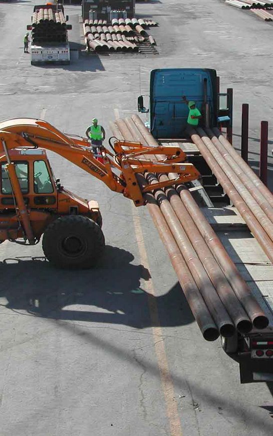 A tractor is parked next to some pipes.