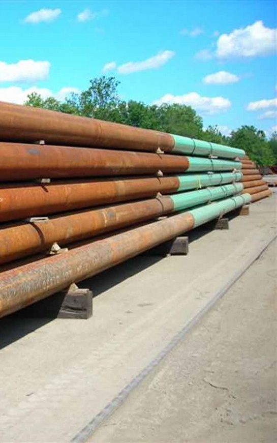 A bunch of pipes are stacked up on the side of the road.