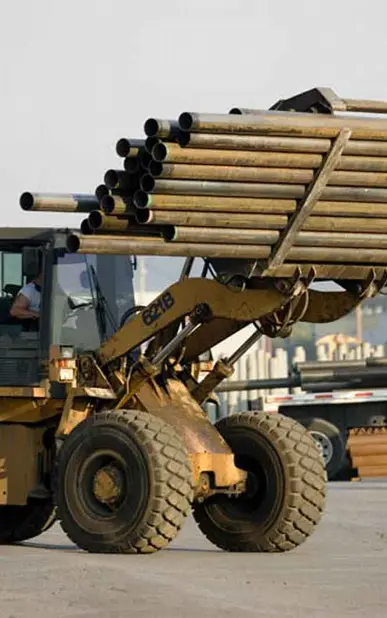 A large yellow tractor with a load of pipes on it's back.