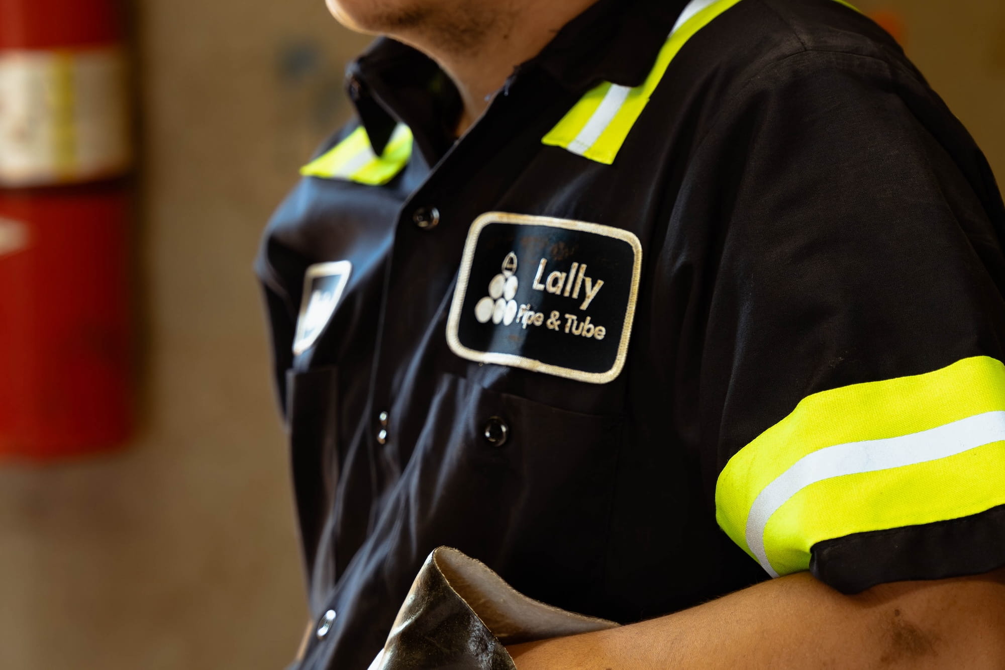Close-up of a Lally Pipe and Tube employee uniform shirt with embroidered company logo patch and hi-vis safety reflective strips