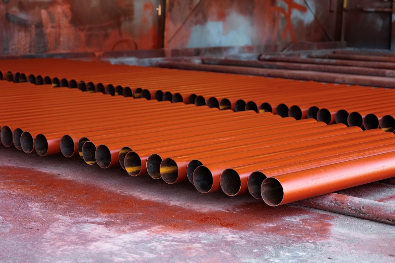 Several pipes with a red coating sitting on the floor in a long row