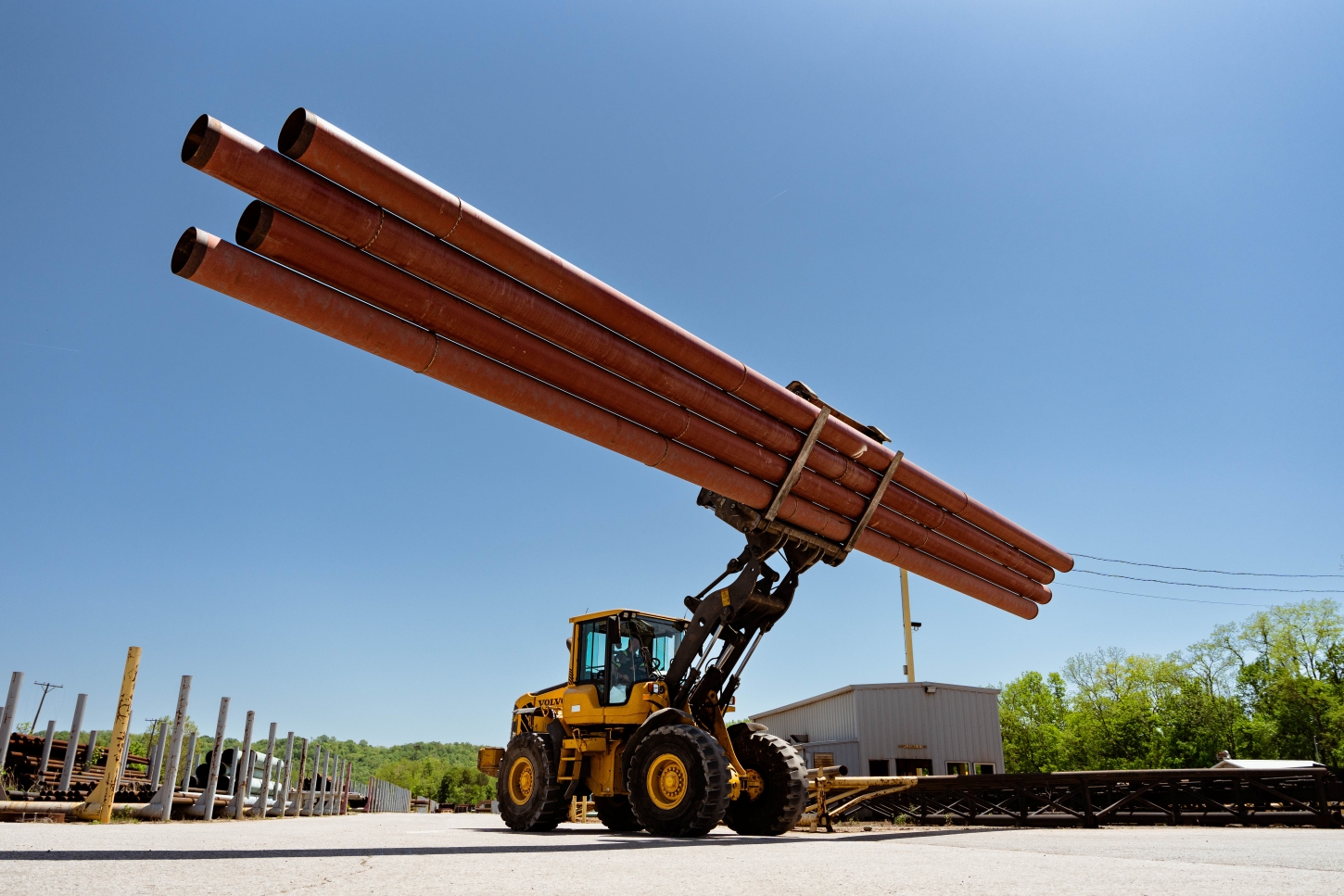 Outdoor photo of a forklift holding up several long pipes