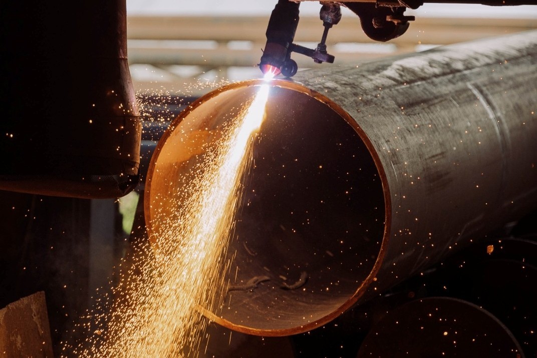 Close up of a machine cutting a large pipe, with lots of sparks flying